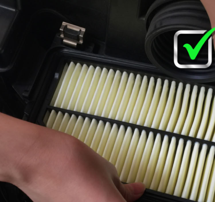 Deux mains installant un filtre à air dans un compartiment de moteur, avec une coche verte visible.